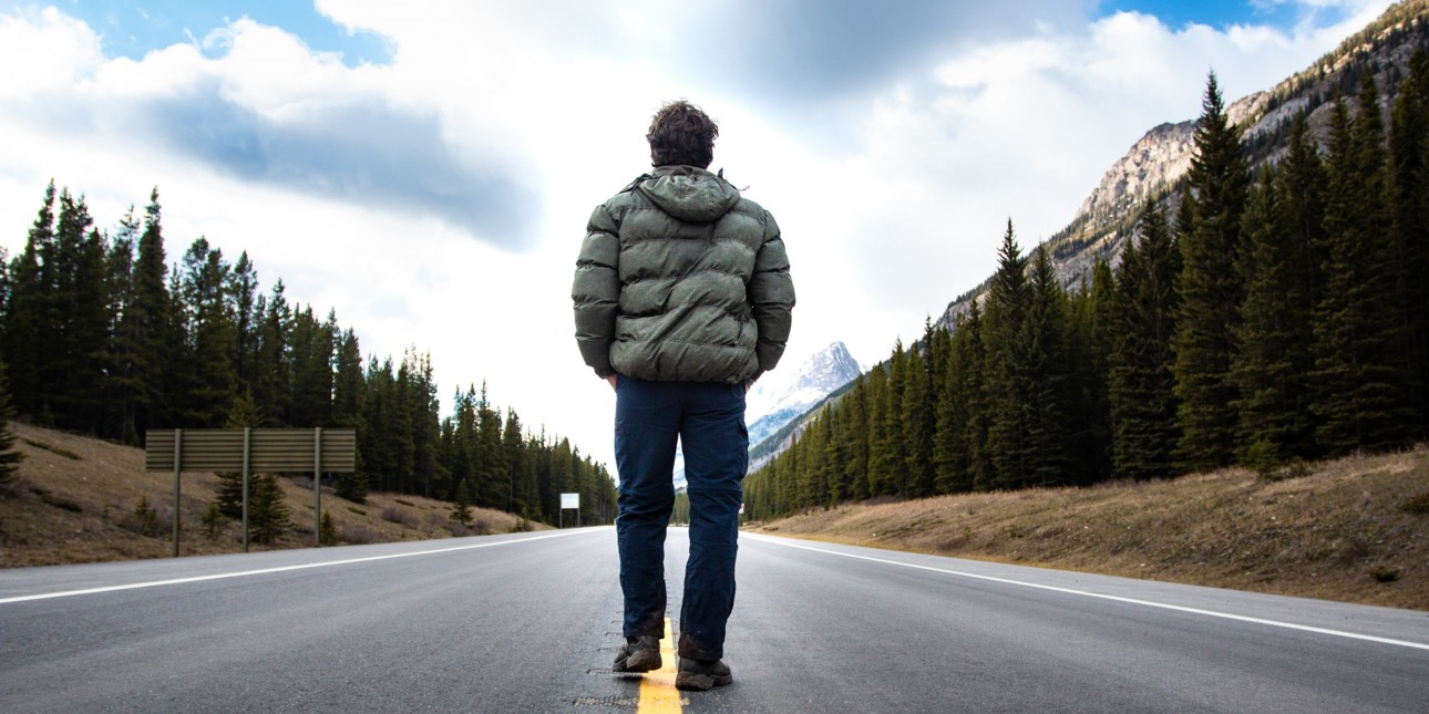 person wearing coat walking down mountainous street