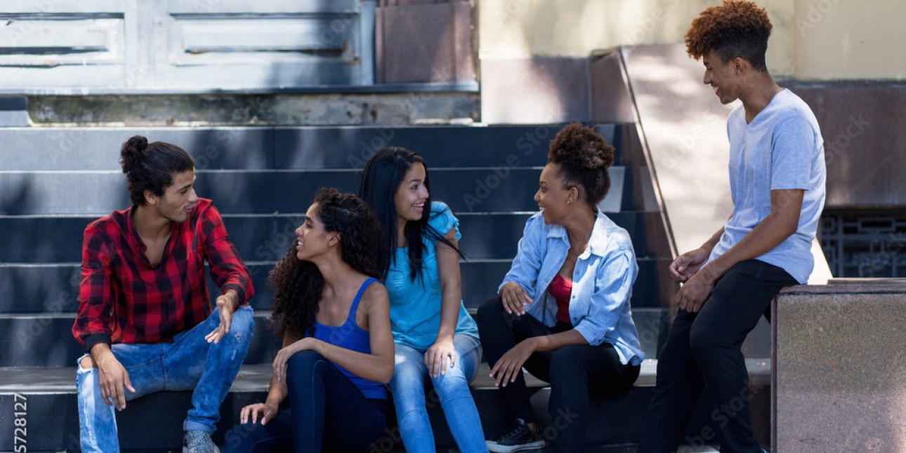 Latinx youth talk together on steps outside a home.