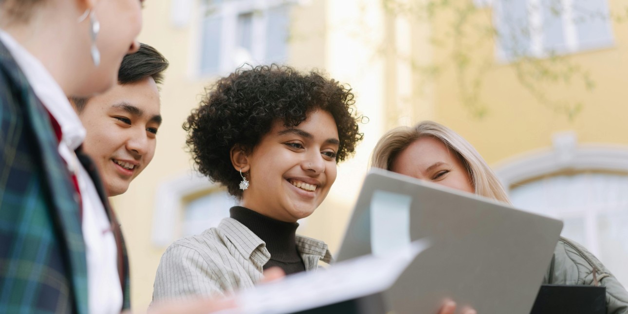 A woman and colleagues look at a laptop screen outdoors.