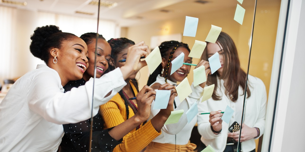 Black women write on Post-It notes stuck to glass