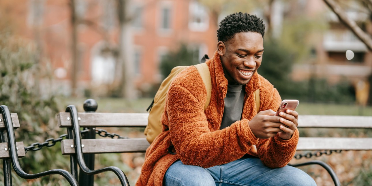 a Black man looking at his phone on a park bench