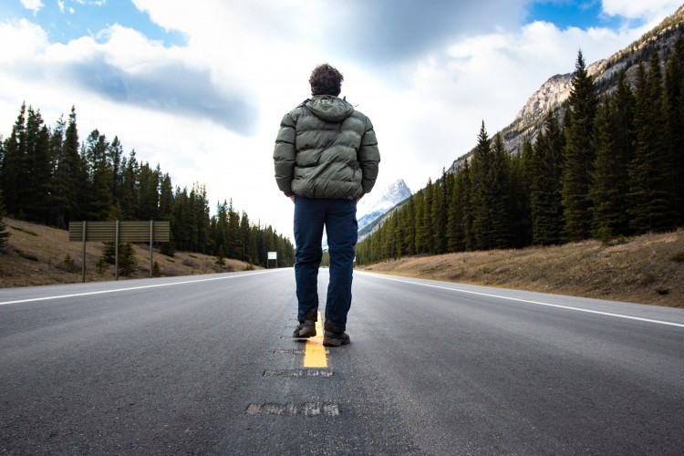 person wearing coat walking down mountainous street