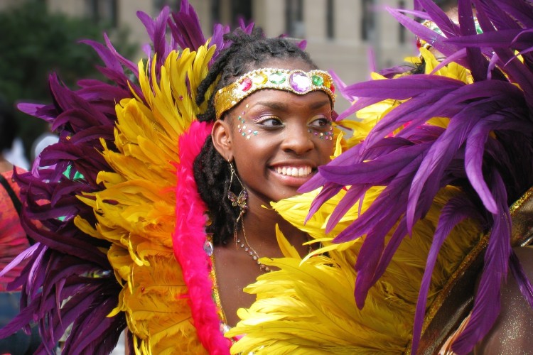 A young Black woman in feathered costume during a Caribbean day festival.