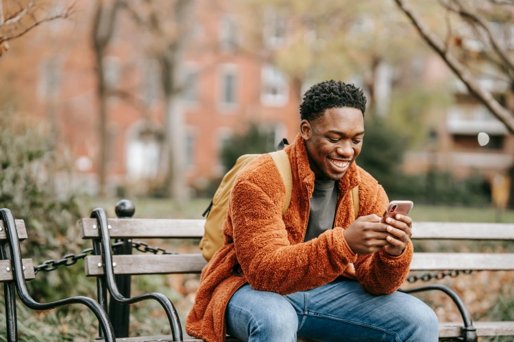 a Black man looking at his phone on a park bench