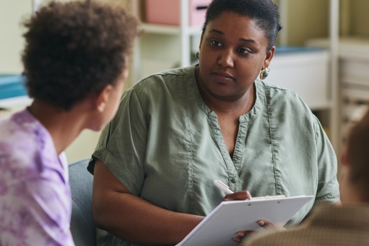 A woman listen and takes notes while a young man talks with her